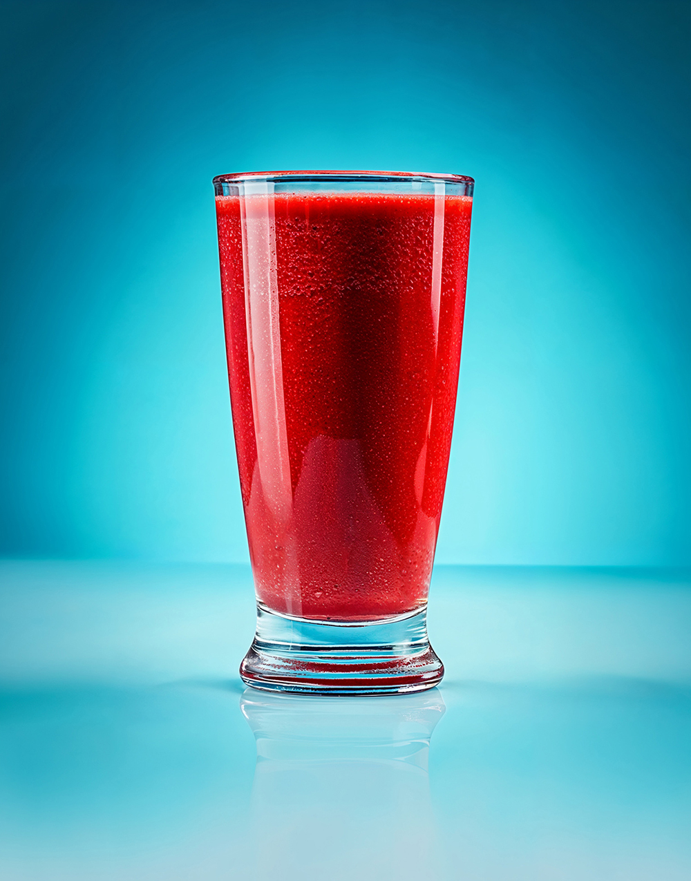 Schmuckbild Getränke. Glas mit Tomatensaft vor blauem Hintergrund