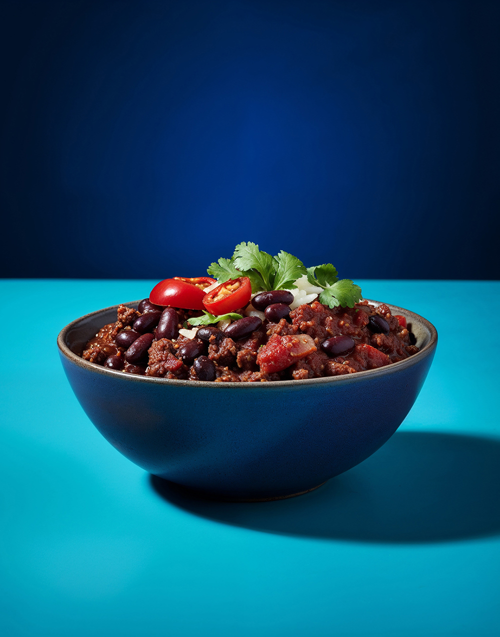 Schmuckbild Chilie con Carne in einer blauen Keramikschüssel vor blauem Hintergrund